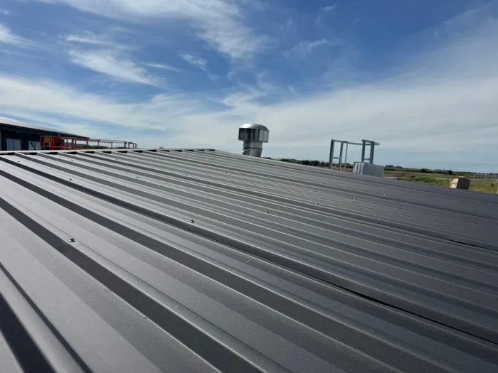 The finished roof sheeting on a tank, fixings in rows, a turbine vent standing at the ridge