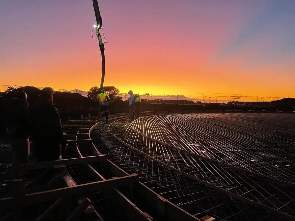 Reinforcing steel laid for a tank foundation at sunset, crew working