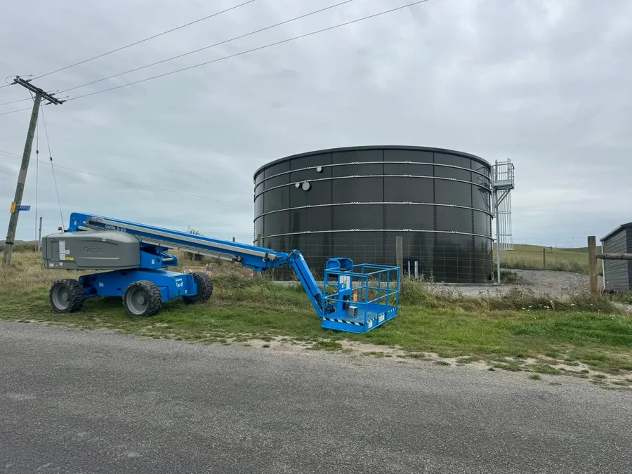 A boom lift set up beside a bolted steel tank for access work