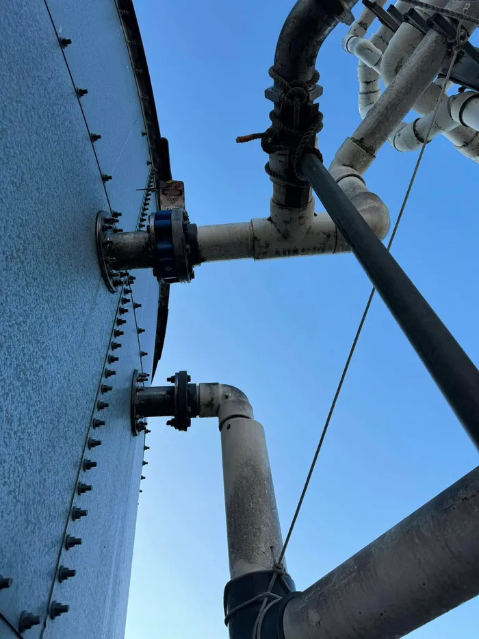 External pipework reconnected to the flanges on the tank wall, seen from the ground against a clear sky