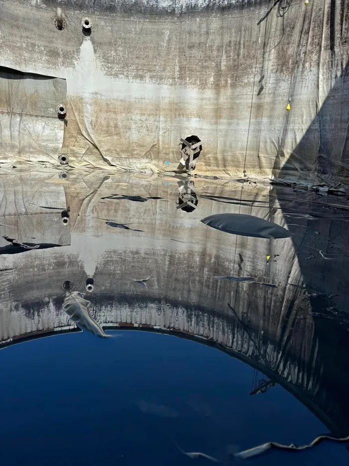 The failed old liner inside the tank, split and slumped, holding standing water across the floor