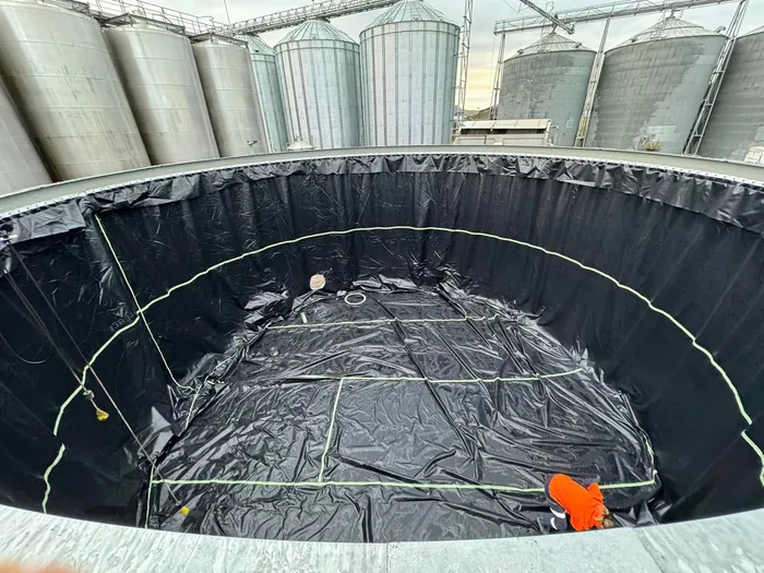 The new black liner laid out across the tank floor, a crew member working the edge into the wall