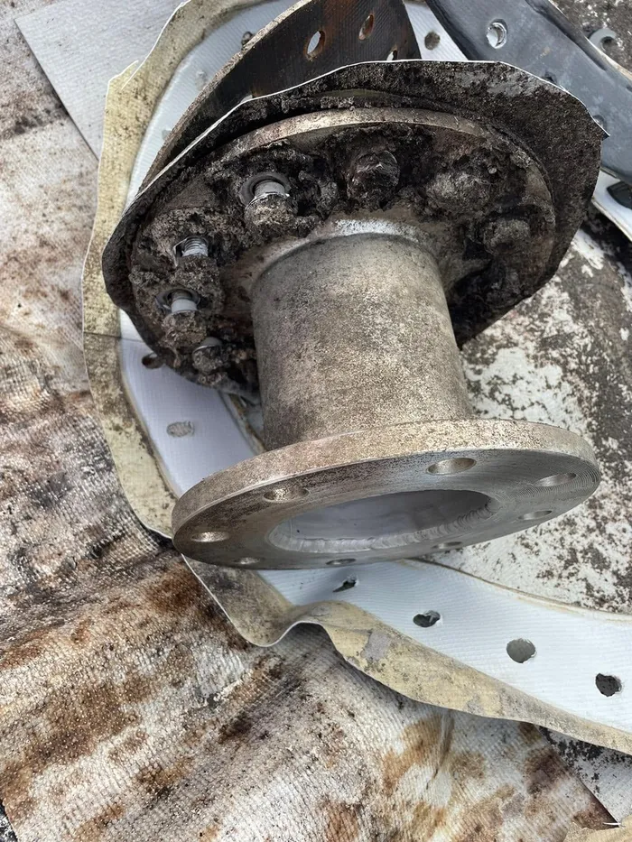 A heavily corroded outlet flange cut out of the tank, resting on the old liner it came through