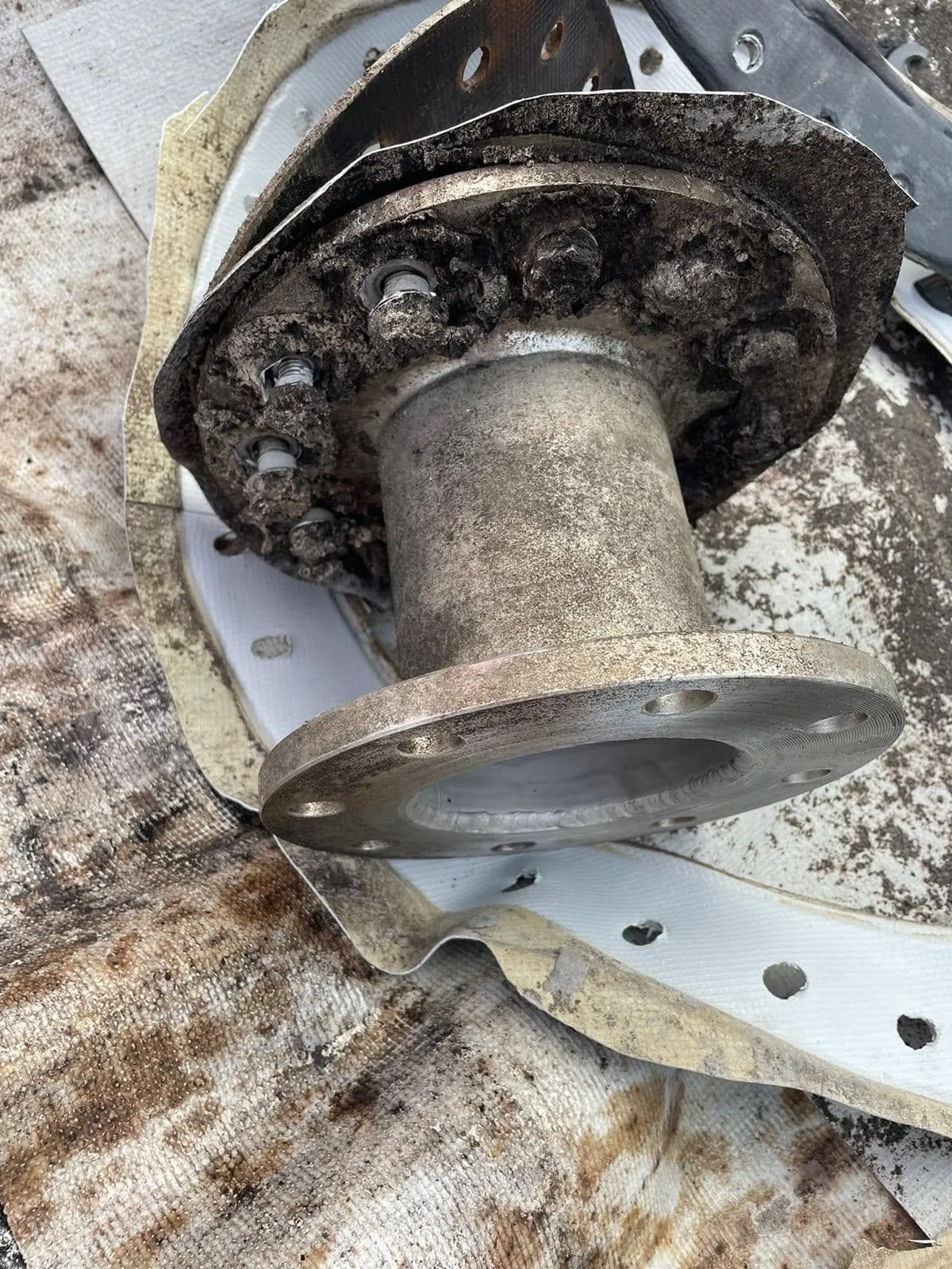 A heavily corroded outlet flange removed from a tank during a repair, resting on the old liner