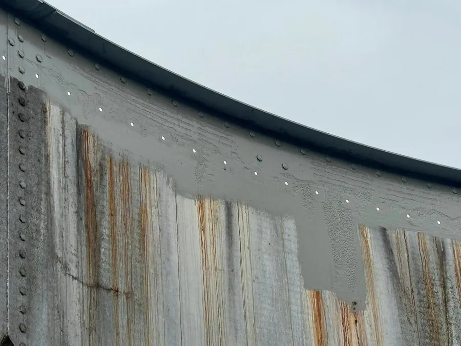 Rust streaking down a weathered tank wall, with fresh coating going on above it